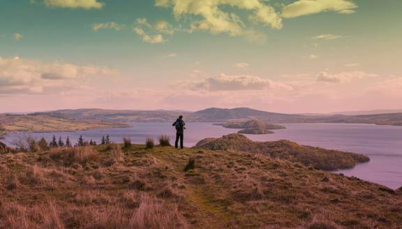 A lone hiker takes in the view across Loch Lomond from the summit of Conic Hill. Islands dot the placid water