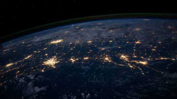 The earth seen from space. It is night on the planet's surface and urban and street lighting glitters from below like a string of pearls