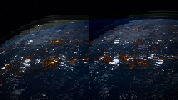 The earth seen from space. It is night on the planet's surface and urban and street lighting glitters from below like a string of pearls