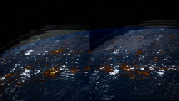 The earth seen from space. It is night on the planet's surface and urban and street lighting glitters from below like a string of pearls