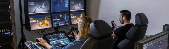 ROVOP staff using the ROVOP Academy training simulator. Two people using joysticks and touchscreens sit in front of a bank of monitors