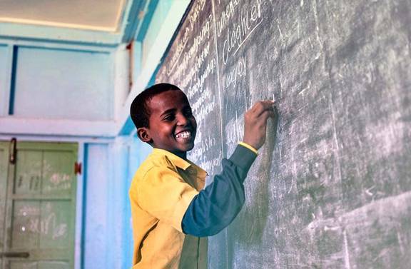 Child in African classroom writing on blackboard