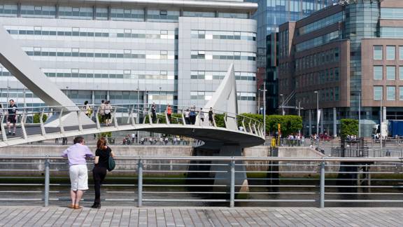 People walk across a footbridge over the River Clyde in Glasgow in bright Spring sunshine