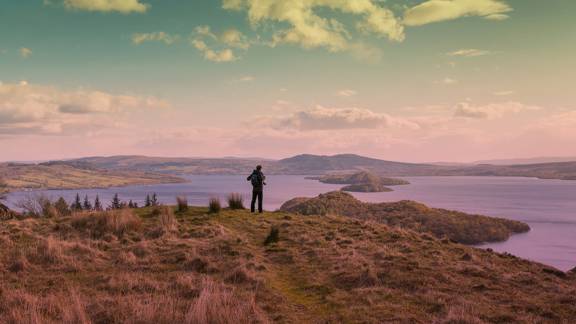 A lone hiker takes in the view across Loch Lomond from the summit of Conic Hill. Islands dot the placid water