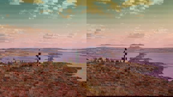 A lone hiker takes in the view across Loch Lomond from the summit of Conic Hill. Islands dot the placid water