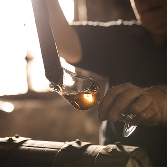 Man extracting a sample of whisky from a cask in to a glass